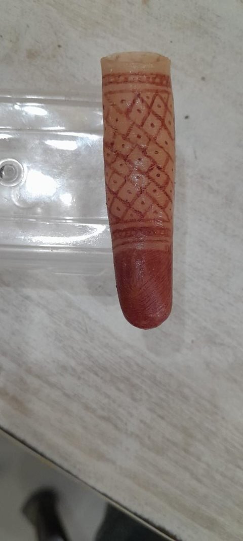 A single silicone finger prosthesis decorated with a fine lattice mehndi pattern and a solid darkened fingertip