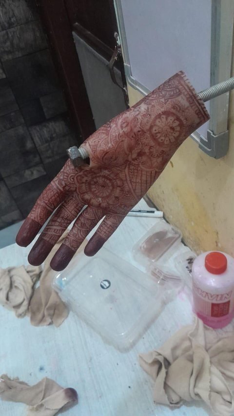 Mehndi-decorated silicone hand prosthesis held on a threaded fixture, showing the dense circular palm design and darkened fingertips