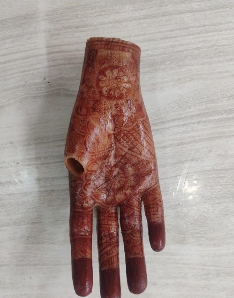 Silicone hand prosthesis covered in a detailed reddish-brown mehndi design across the back of the hand and down each finger