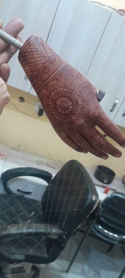 Mehndi-decorated silicone hand and wrist prosthesis on a workshop fixture, the design running from the forearm cuff to the fingertips
