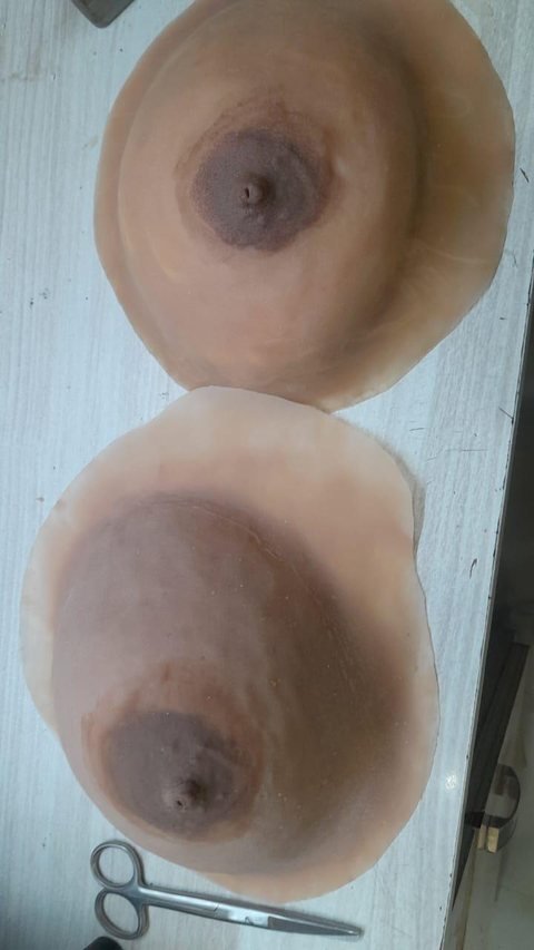 Two external silicone breast prostheses with formed nipple and areola, lying on a work surface