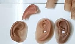 Four silicone ear prostheses in different skin tones laid on a white surface, showing the formed helix, antihelix and lobe of each