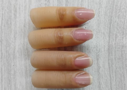 Four silicone finger prostheses laid in a row, each with a formed nail bed, pink nail and fine skin creases along the digit