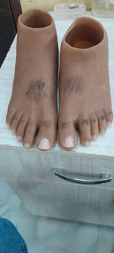 Pair of silicone foot prostheses showing implanted hair on the top of each foot and across the toes, with formed toenails