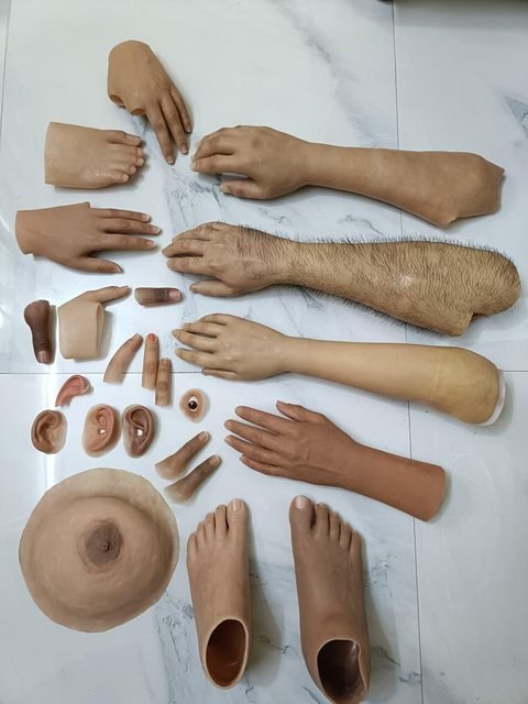 A full range of silicone prostheses laid out together — hands, arms, fingers, ears, an eye, a breast form and a pair of feet in a variety of skin tones